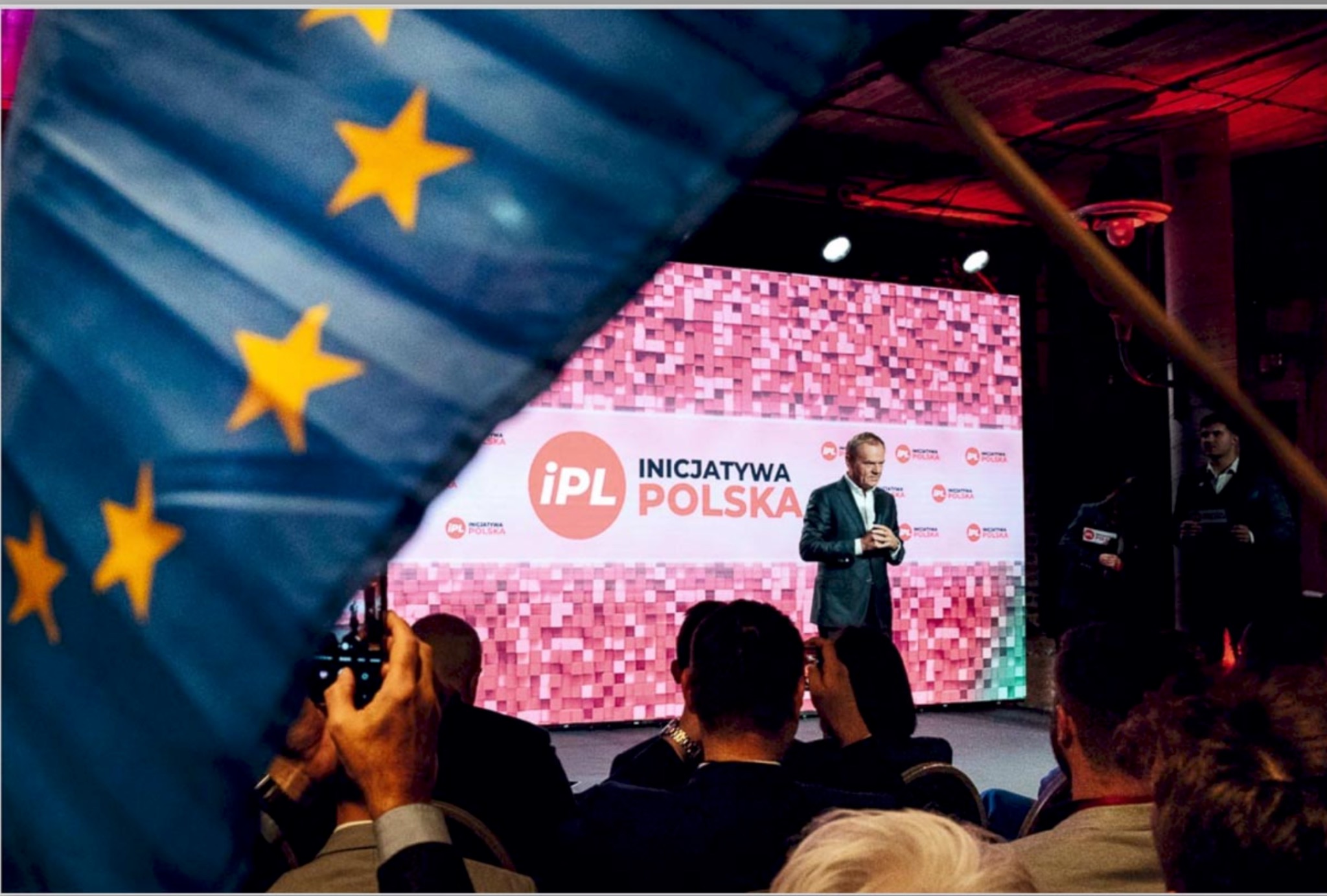 Conference speaker on stage with EU flag in foreground